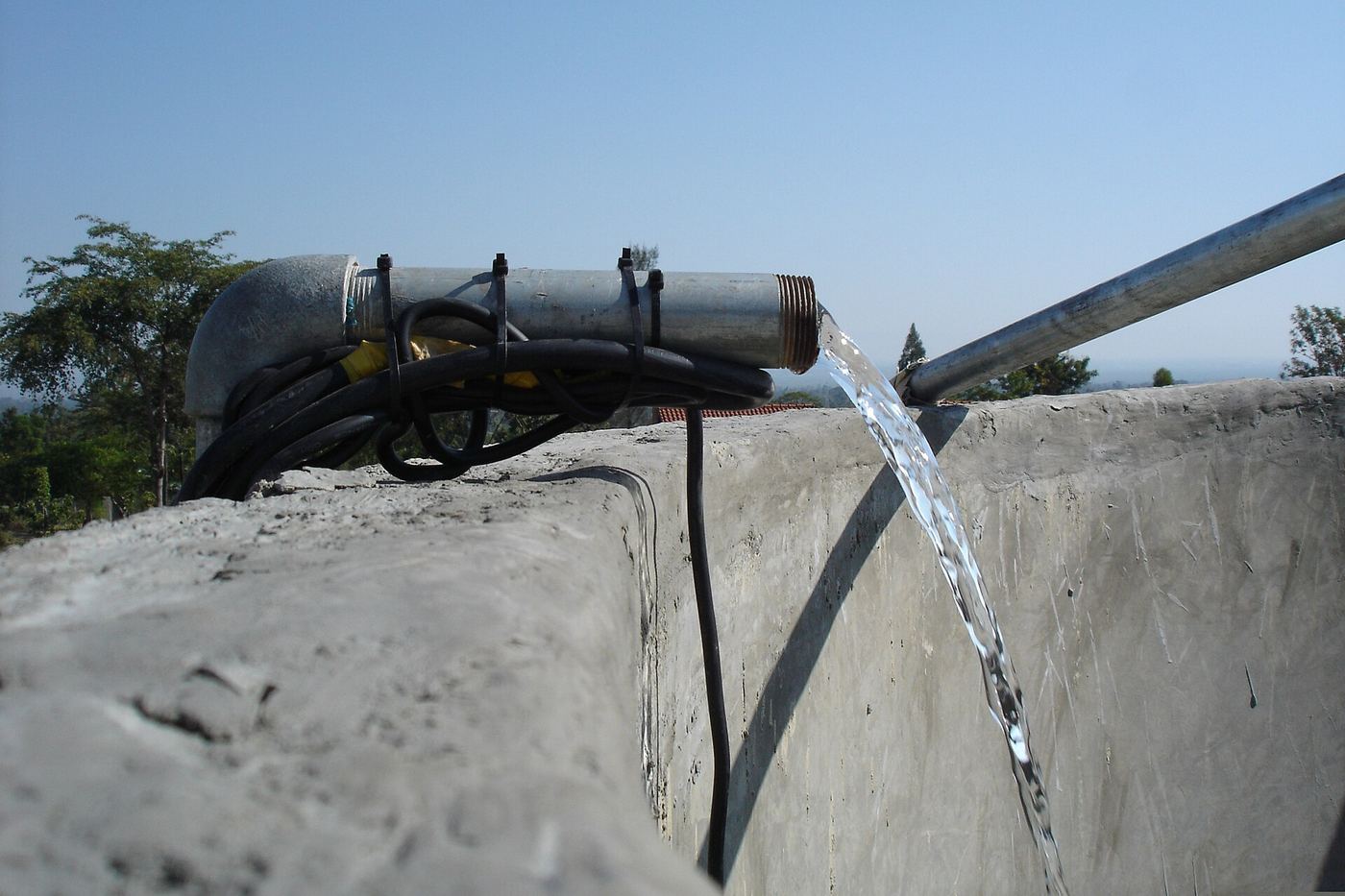 L’eau d’une pompe solaire jaillit d’un tuyau dans un bassin en béton. Le câble de la pompe est enroulé sur le tuyau.